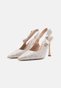 Slingback-korkokengät vaaleassa beigestä, joissa on kimaltava kristallikoriste, teräväkärkinen muoto ja teksturoidusta kankaasta valmistettu nauha nilkassa.