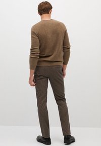 Suéter de lana marrón con texturas acanaladas, combinado con pantalones oscuros de cuadros. La modelo está de espaldas, mostrando la parte trasera del conjunto.