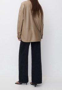 Chemise en cuir beige surdimensionnée avec une couture au dos, associée à un pantalon large noir taille haute et des sandales à talons noires.