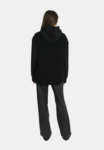 Felpa nera con cappuccio in tessuto testurizzato, vestibilità ampia e maniche lunghe, abbinata a pantaloni grigi a zampa d'elefante. Design pulito e semplice.