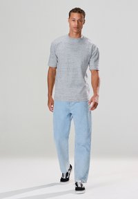 Grijs T-shirt met korte mouwen en een gestructureerd patroon, gecombineerd met lichtblauwe, loszittende jeans en zwarte sneakers met witte accenten.