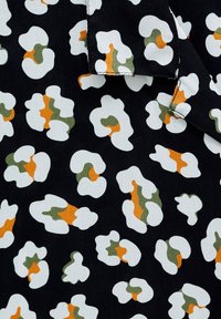Black fabric featuring an abstract camouflage pattern in white, green, and orange shapes. The texture appears smooth and lightweight.