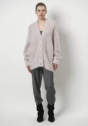 Helle rosa, flauschige Strickjacke mit V-Ausschnitt und Fünf-Knopf-Verschluss. Hat übergroße Ärmel und eine lockere Passform, kombiniert mit grauen Hosen.