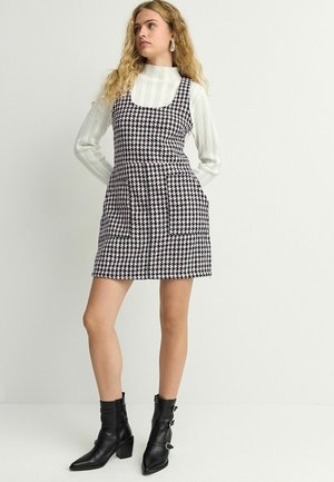 Abito senza maniche a scacchi in bianco e nero con motivo houndstooth, con vita aderente e tasche laterali, abbinato a stivaletti neri alla caviglia.