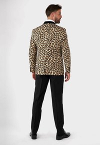 Blazer con stampa leopardata e dettagli neri, design monopetto e tessuto liscio abbinato a pantaloni e scarpe neri.