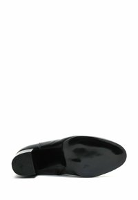 Chaussure en cuir noir avec un bout arrondi, texture lisse, design minimal et semelle en caoutchouc plate dotée de motifs de grip horizontaux.