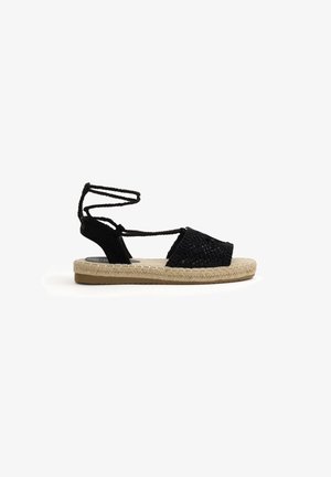 Sandalia espadrille negra tejida con lazo para atar en el tobillo, suela trenzada de yute y plantilla beige acolchada.