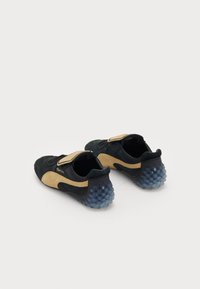 Black and beige athletic shoes with a suede upper, Velcro strap, and a translucent blue rubber sole featuring textured bumps.
