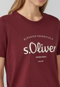 T-shirt en coton bourgogne à manches courtes, avec le texte blanc « s.Oliver » et « Essentials Élevés » en impression graphique.