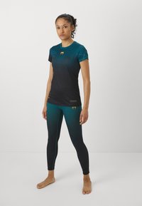 Sportlik topp ja legginsid gradueeruva teal to must värviga. Pehme, veniv kangas, millel on võrkpaneelid ja kuldsed logo aktsendid. Tihedisain.