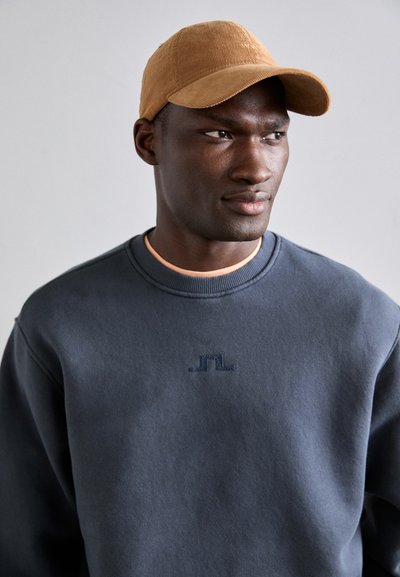 Sweatshirt azul-marinho com logótipo bordado, decote redondo e detalhes em pêssego. Combinado com um boné de basebol em courduroy bege, com aba curvada.
