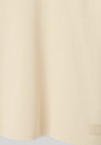 Tissu beige clair à texture lisse, doté d'un ourlet arrondi et d'une petite étiquette embossée dans le coin inférieur droit.