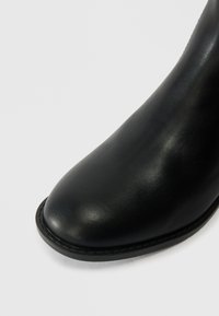 Fekete bőr bokacsizma kerek orral. Simább felület és minimális varrások a talpon. Finom fény a felületen.