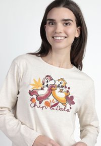 Camiseta de manga larga beige con un gráfico colorido de Chip y Dale rodeados de hojas de otoño, con el texto "Chip & Dale" en rojo debajo de la ilustración.