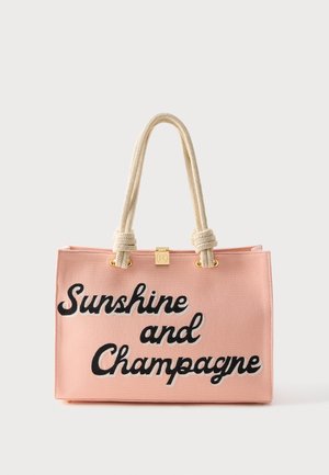 Różowa prostokątna torba typu tote z grubymi kremowymi uchwytami ze sznurka oraz czarnym tekstem pisaną czcionką z napisem „Sunshine and Champagne” z przodu.