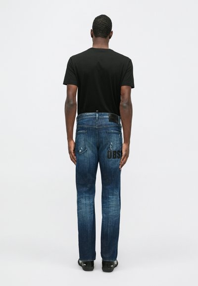 Tmavo modré denimové džínsy s rovnými nohavicami, obsahujúce čiernu koženú nášivku a nápis "OBS" natlačený na zadnej vrecku. Nosia sa s čiernym tričkom.