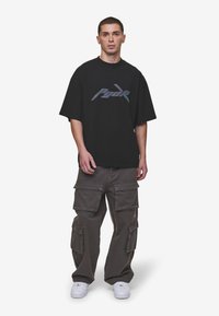Black oversized t-shirt with a reflective logo, paired with loose-fitting gray cargo pants featuring multiple pockets and white sneakers.