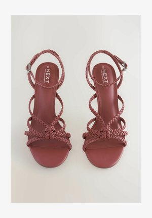 Punased punutud kontsasaapad platvormiga disainiga, millel on mitu omavahel põimunud rihma ja metallist luku, et tagada kohandatav istuvus.