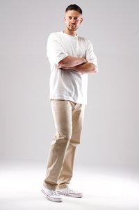 White short-sleeve t-shirt, beige chinos, and white sneakers with red accents. Model stands with arms crossed against a neutral background.