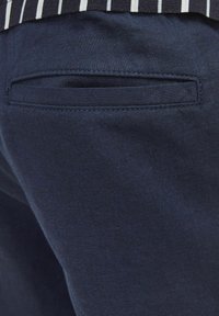 Pantalons en coton marine avec une poche arrière à ouverture horizontale élégante et un subtil détail de couture. Coupe décontractée, texture lisse.