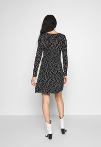 Svart långärmad klänning med vita prickar, åtsittande vid midjan och utställd vid fållen. Buren med ankelstövlar med blockklack.