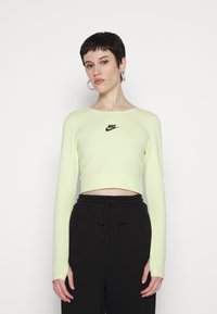 Rövidre vágott, hosszú ujjú ing neon sárga színben, elasztikus anyagból készült, fekete Nike logóval a mellrészen és testhez simuló fazonnal.