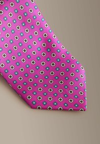 Pink tie featuring a geometric pattern of small squares and floral motifs in white and black, with turquoise accents. Textured fabric.