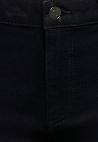 Tissu en denim noir avec un bouton en métal et une couture visible sur la poche avant d'un jean.