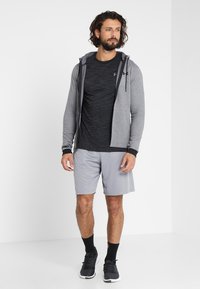 Grijze rits-hoodie over een zwart gestructureerd shirt, gecombineerd met lichtgrijze shorts en zwarte sportschoenen. Eenvoudig ontwerp en casual pasvorm.