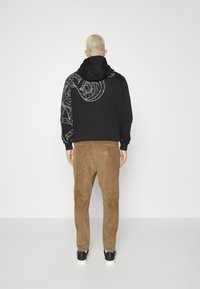 Černá mikina s bílým grafickým vzorem na zádech, spárovaná s hnědými kordovým kalhotami a černými teniskami s bílou podrážkou. Pohled zezadu.