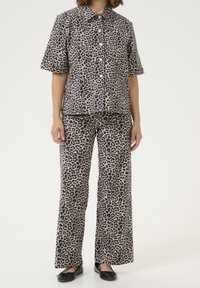 Set in due pezzi con stampa leopardata composto da una camicia a maniche corte con bottoni e pantaloni a gamba larga in tonalità beige e nera, realizzato in un tessuto morbido e con una texture liscia.
