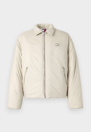 Bež jakna s punjenjem s uspravnim ovratnikom, prednjim patentnim zatvaračem i dva bočna džepa. Sadrži logo oznaku na lijevoj strani prsnog koša.