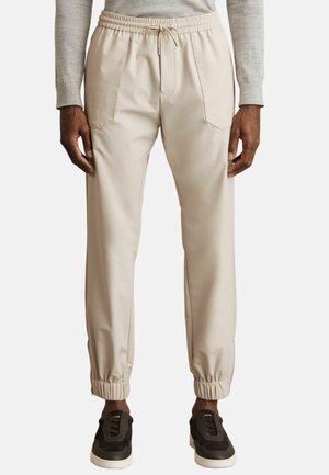 Pantaloni jogger bej cu talie elastică, buzunare laterale și mansete îngustate. Materialul are o textură netedă și un design minimalist.