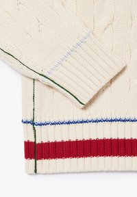 Manche et ourlet d'un pull en maille crème avec poignets côtelés et détails rayés rouges, bleus et verts.