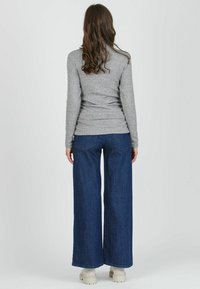 Grau gestreiftes Langarmoberteil kombiniert mit weit geschnittenen, dunklen Jeans und beigen Plateau-Schuhen. Glattes Material und lockere Passform.