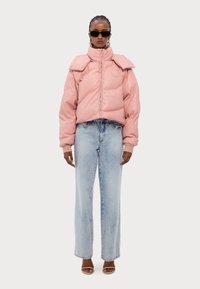 Rosa puffjacka med vikbar krage och framdragkedja, kombinerad med ljusblå raka jeans. Modellen bär svarta solglasögon och sandaler med remmar.