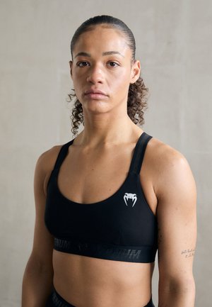 Black sports bra with logo, featuring a round neckline and thin straps. Smooth texture and elastic band with branding detail.