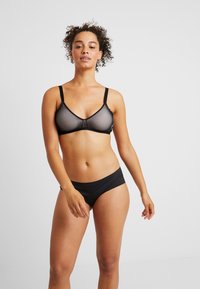 Černá podprsenka a odpovídající bikiny vyrobené z hladkého materiálu. Podprsenka má síťovaný design bez drátků a nastavitelné ramínka.