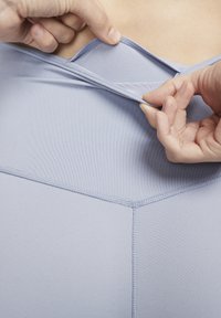 Tessuto di un viola chiaro con una texture liscia, caratterizzato da un design a zigzag nelle cuciture. Le mani stanno regolando il capo all'altezza del collo.