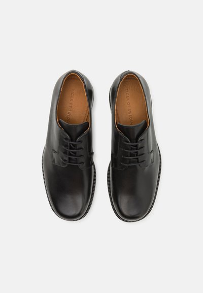 Scarpe eleganti in pelle nera con superficie liscia, dotate di punte arrotondate e un interno in pelle marrone a contrasto. Lacci e suole texturizzate.