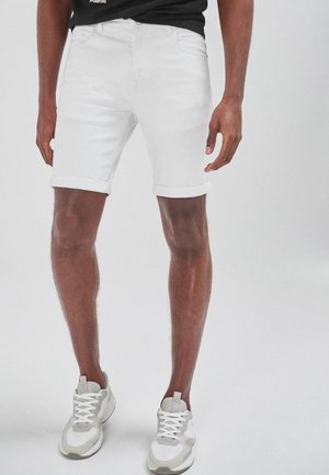 Shorts en denim blanc avec des ourlets retroussés, présentant un design classique à cinq poches. Assortis avec des baskets de sport grises et blanches.