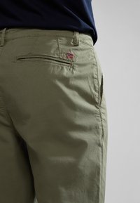 Pantalones cortos caqui con textura suave, que presentan un bolsillo trasero y un pequeño detalle de la bandera noruega. Diseñados con un corte recto y presillas para cinturón.