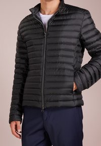 Svart vadderad jacka med dragkedja, featuring en ståkrage och horisontell quiltad yta. Slim fit med sidofickor.