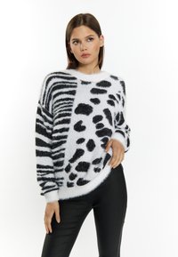 Weißer, flauschiger Pullover mit kontrastierenden schwarzen Tiermuster-Designs, einschließlich Streifen und Punkten, im entspannten Schnitt und mit rundem Ausschnitt.