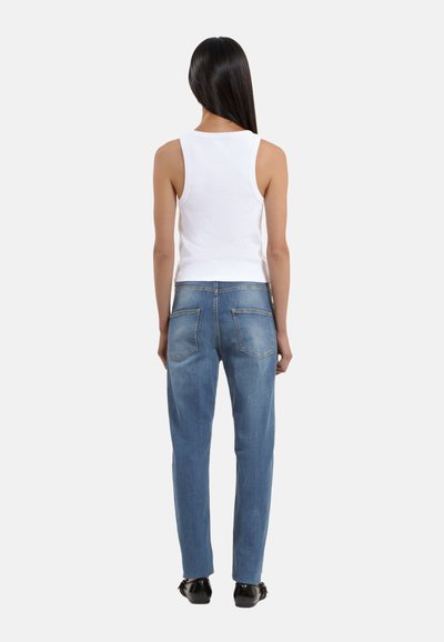 Witte geribbelde tanktop gecombineerd met lichtblauwe rechte jeans. De jeans hebben achterzakken en een gladde textuur. Model kijkt van de camera af.