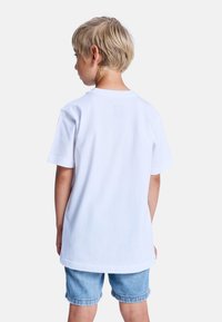 Weißes Baumwoll-T-Shirt mit kurzen Ärmeln und rundem Ausschnitt, kombiniert mit Denim-Shorts. Die Rückansicht zeigt eine lockere Passform und ein einfaches Design.