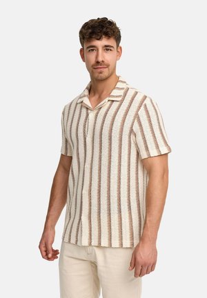 Mann trägt kurzärmeliges Strickhemd mit vertikalen beigen und braunen Streifen, steht vor einem schlichten hellen Hintergrund.