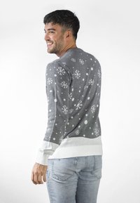 Grauer Pullover mit weißen Schneeflocken- und Punktmustern, gerippter weißer Saum und Bündchen, getragen mit hellblauen Jeans, von hinten gezeigt.