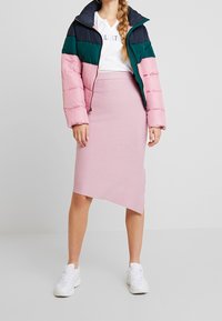 Barevná naducaná bunda s blokovým designem v námořnické modři, zelené a růžové; kombinovaná s přiléhavou asymetrickou světle růžovou sukní a bílými teniskami.