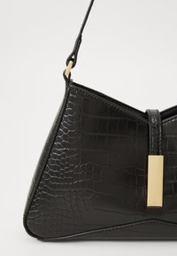 Borsa in pelle patinata nera con texture a coccodrillo, forma triangolare e un'apertura rettangolare in tono oro. Cintura regolabile per la spalla.